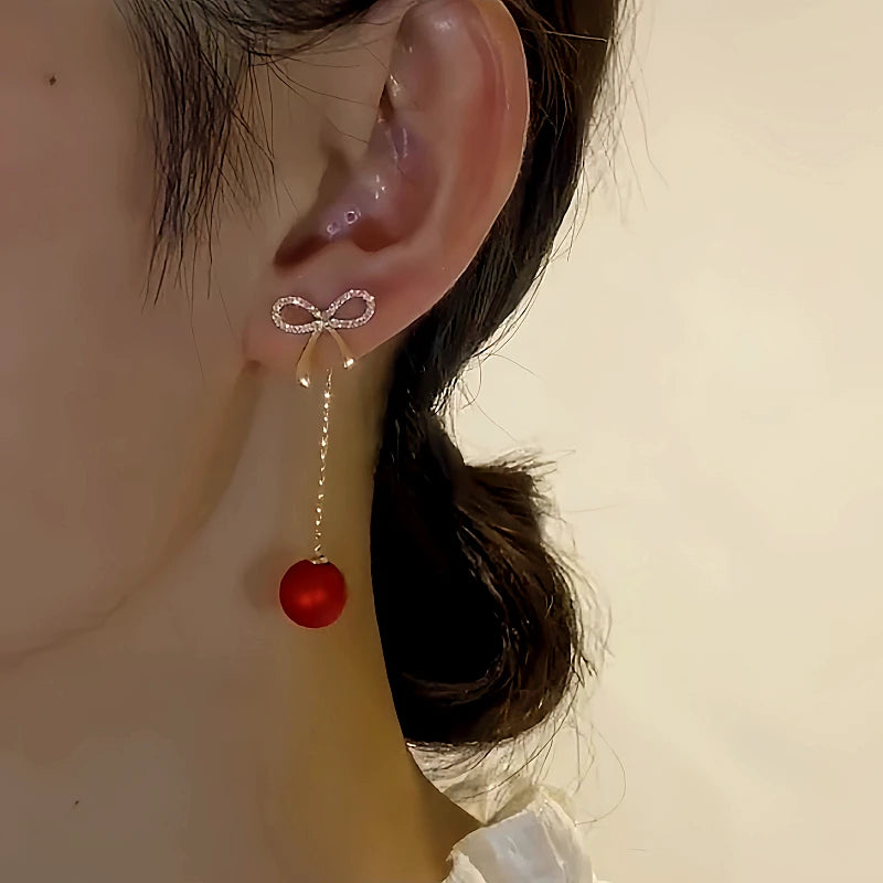 Model showcasing the dangle and style of the 14K Gold-Plated Elegant Zircon Bow Red Pearl Tassel Earrings