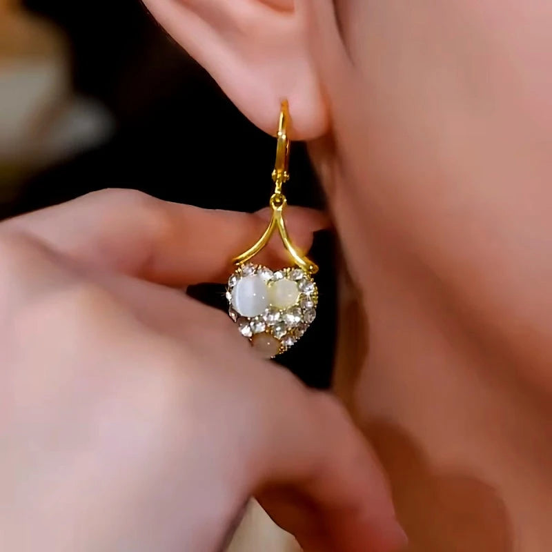 Model showcasing the dangle and style of the 14K Gold-Plated Elegant Zircon Diamond White Cat's Eye Stone Heart Earrings