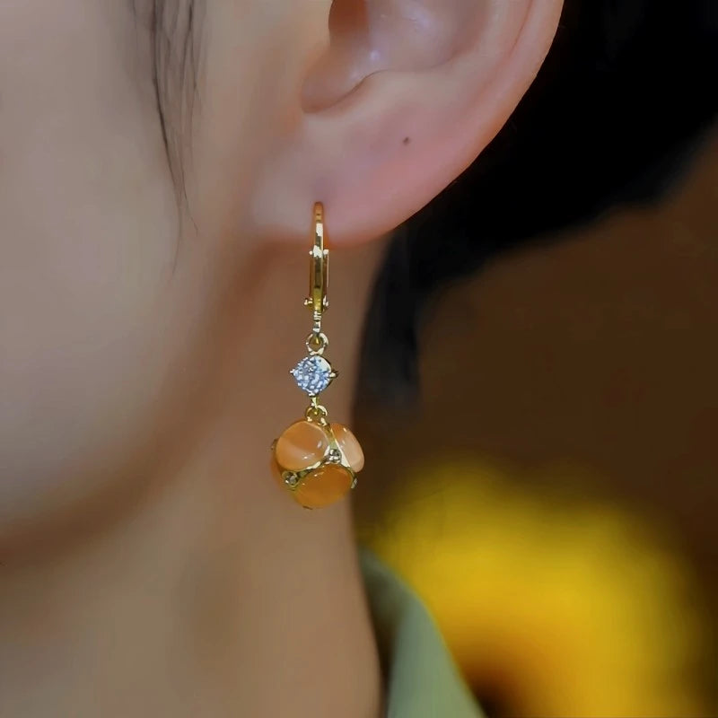 Model showcasing the dangle and style of the 14K Gold-Plated Elegant Zircon Orange Ball Earrings