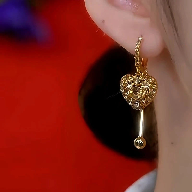 Model showcasing the dangle and style of the 14K Gold-Plated Exquisite Crystal Heart Tassel Earrings