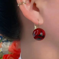Model showcasing the dangle and style of the 14K Gold-Plated Exquisite Smudged Red Ball Earrings