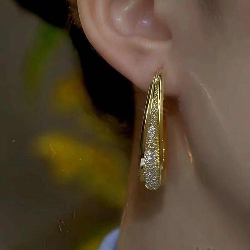 Close-up of gold shimmer oval hoop earring worn on a woman's ear