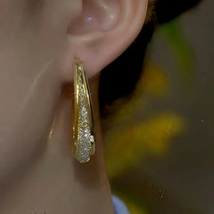 Side view close-up of gold textured oval hoop earring on female ear
