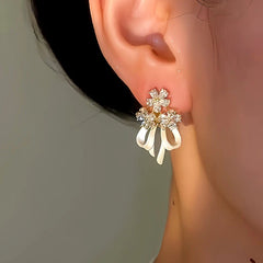 Model showcasing the dangle and style of the 14K Gold-Plated Flower Bow Ribbon Earrings