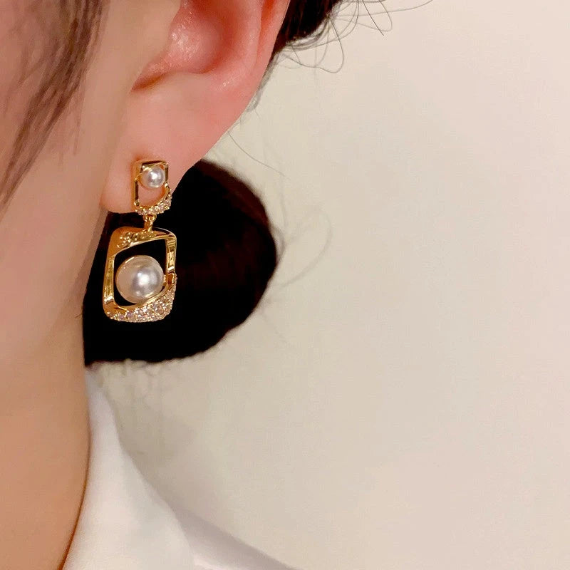 Model showcasing the dangle and style of the 14K Gold-Plated Geometric Pearl Earrings