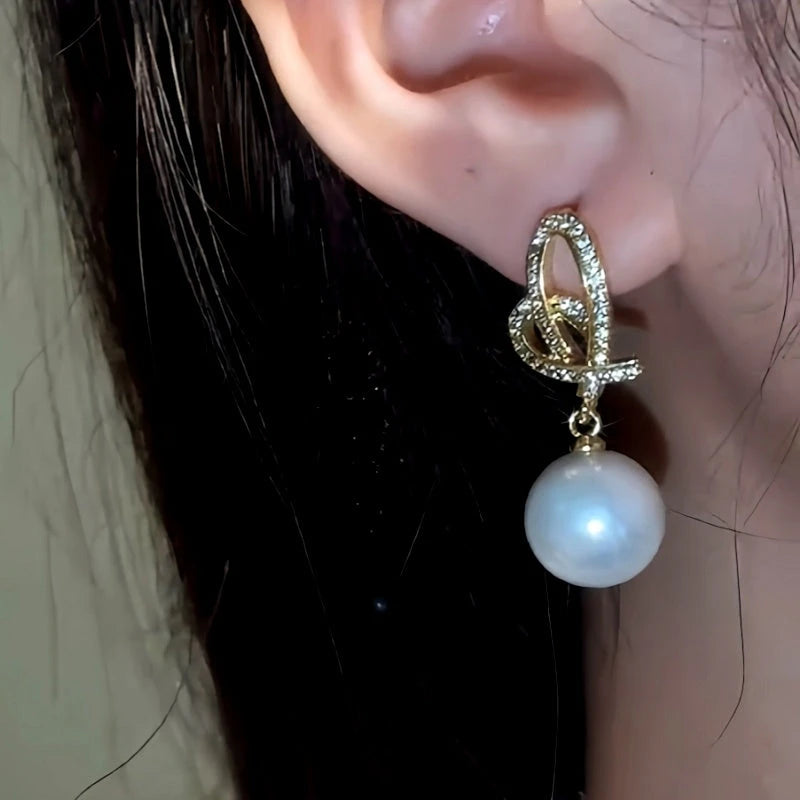 Model showcasing the dangle and style of the 14K Gold-Plated Hollow Heart Pearl Earrings