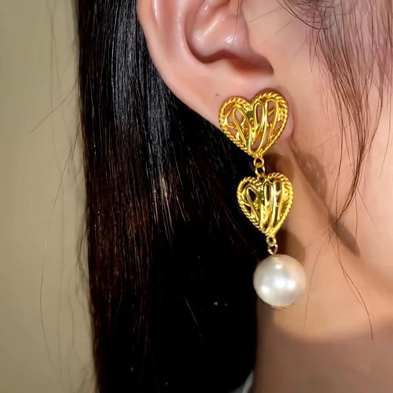 Model showcasing the dangle and style of the 14K Gold-Plated Hollow Twisted Heart Pearl Earrings