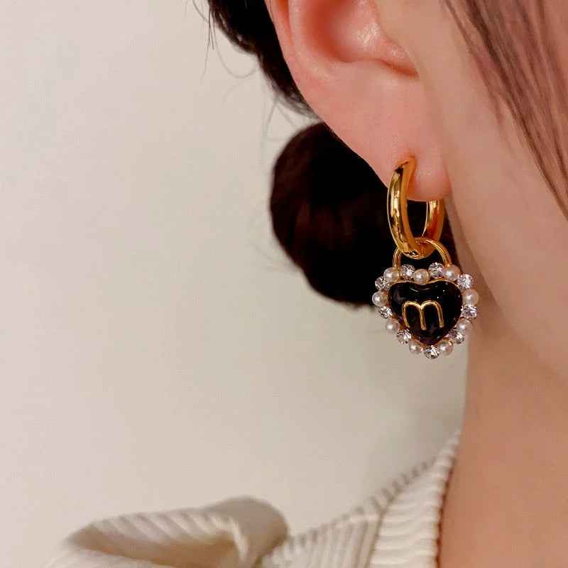 Model showcasing the dangle and style of the 14K Gold-Plated Letter M Black Heart Earrings