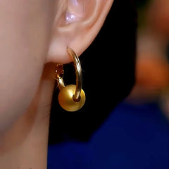 Model showcasing the dangle and style of the 14K Gold-Plated Luxury Brushed Ball Hoop Earrings