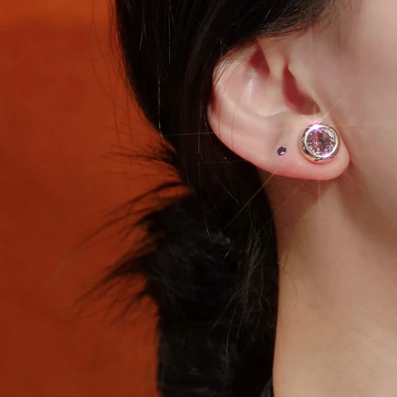 Gold pink round stud earring worn on earlobe with small purple piercing