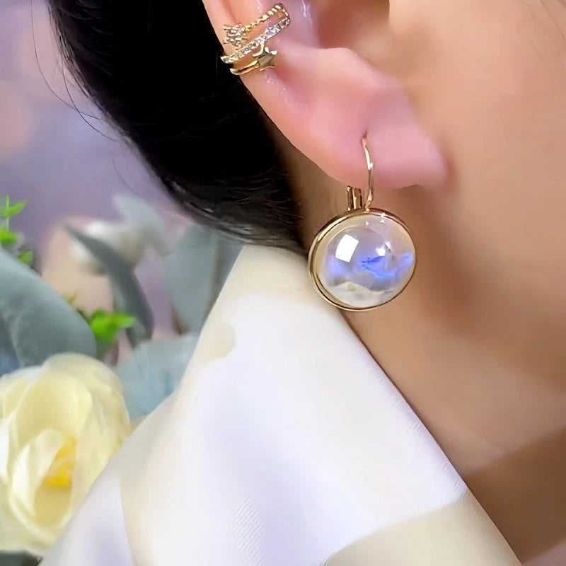 Side view of gold round iridescent blue glass drop earring on ear