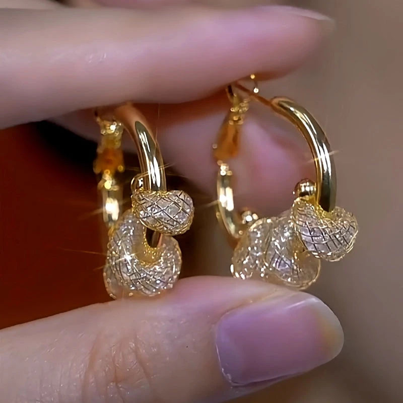 Pair of gold dangle hoop earrings with sparkling mesh crystal charms held by fingers