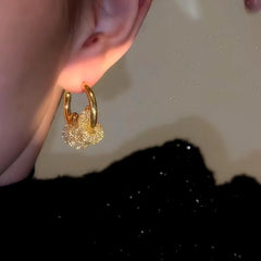 Gold sparkly cluster hoop earring worn on ear, side close-up view