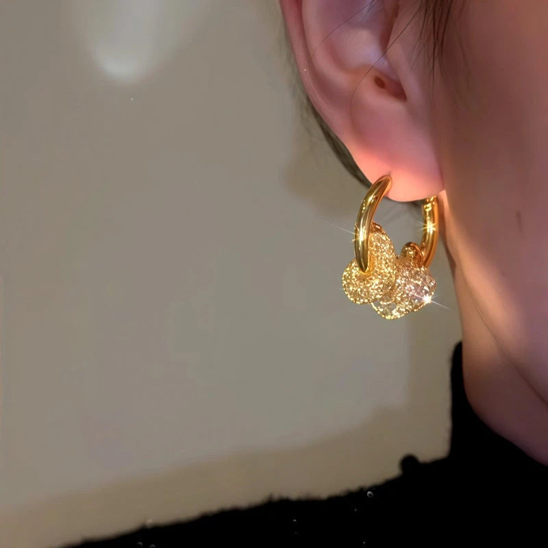Gold shimmering glitter charm hoop earring worn on ear, angled close-up