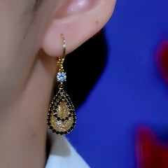Close-up of gold teardrop crystal drop earring with black accents on ear