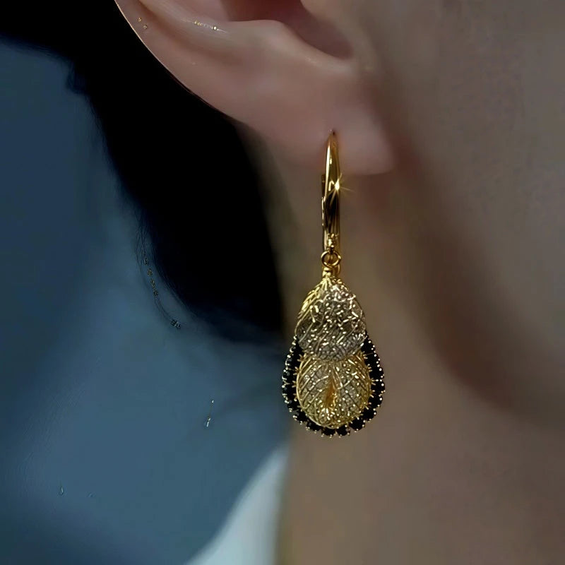 Gold two-tier textured teardrop hoop dangle earring worn on woman's ear, close-up