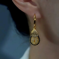Gold two-tier textured teardrop hoop dangle earring worn on woman's ear, close-up
