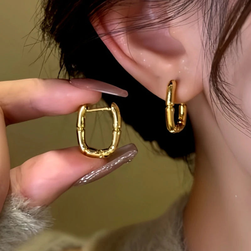 Gold square bamboo hoop earring held beside ear with matching earring worn