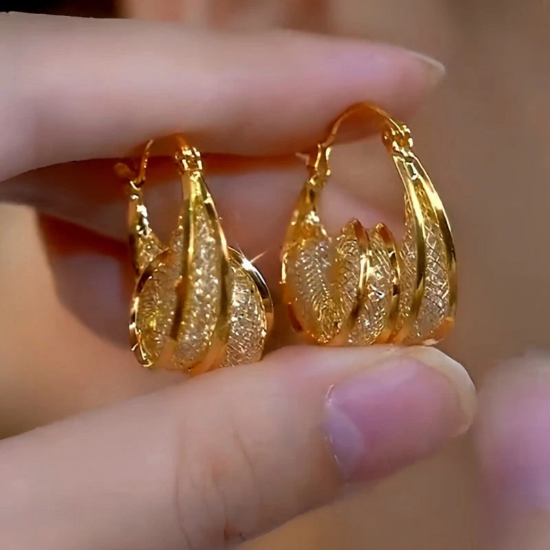 Pair of layered twisted textured gold teardrop hoop earrings held in hand