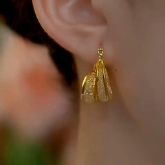 Twisted textured gold teardrop hoop earring worn on a woman's ear