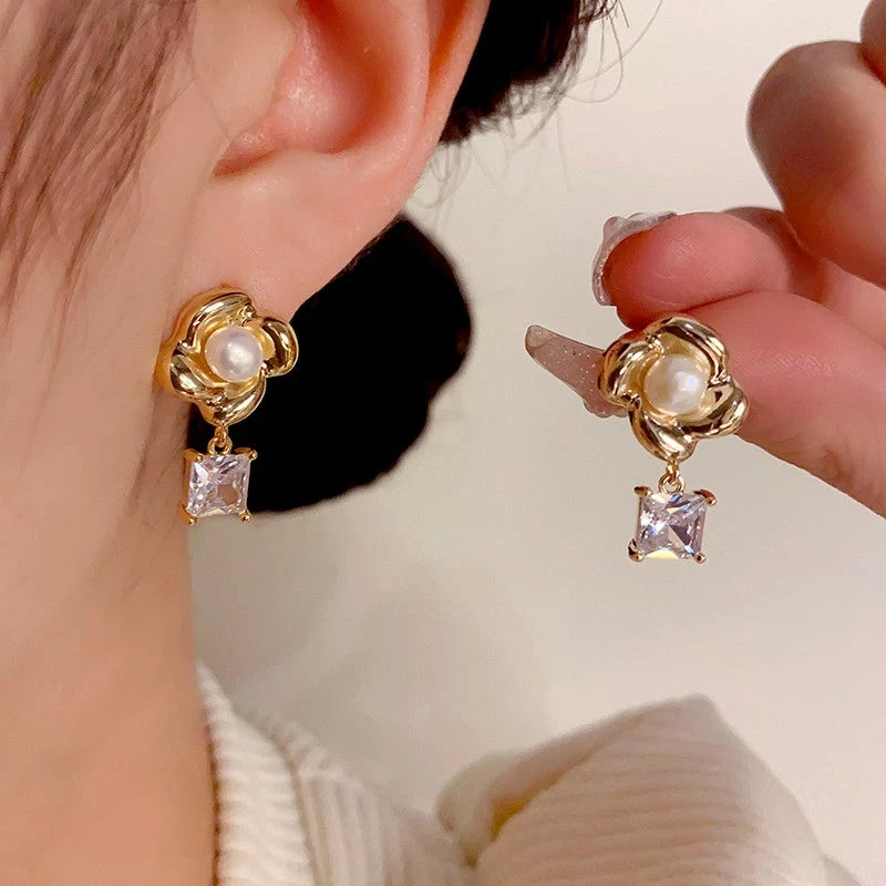 Gold flower pearl square crystal drop earrings: one worn on ear, one held by hand
