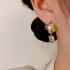 Close-up of gold flower pearl drop earring with square crystal worn on ear