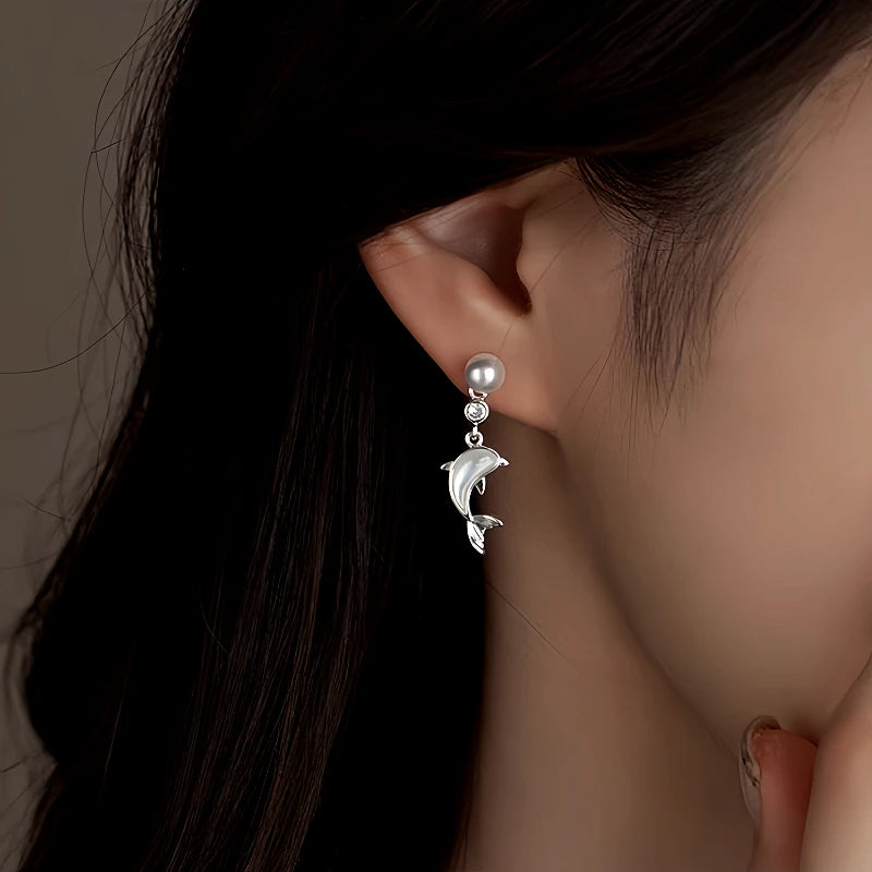 Silver pearl dolphin drop earring worn on woman's ear close-up