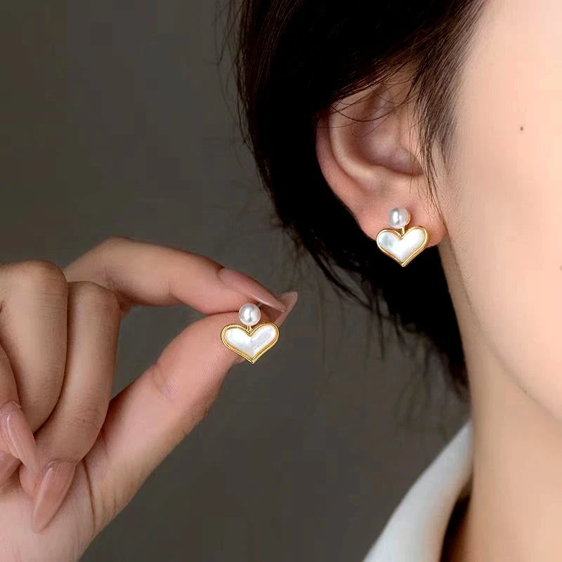 Gold mother of pearl heart stud earrings with pearl accent, woman wearing one and holding another