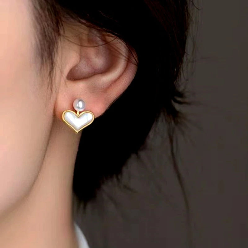 Close up of gold mother of pearl heart stud earring with pearl accent on woman's ear