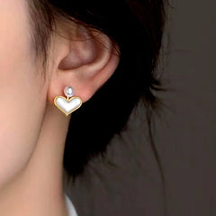 Close up of gold mother of pearl heart stud earring with pearl accent on woman's ear