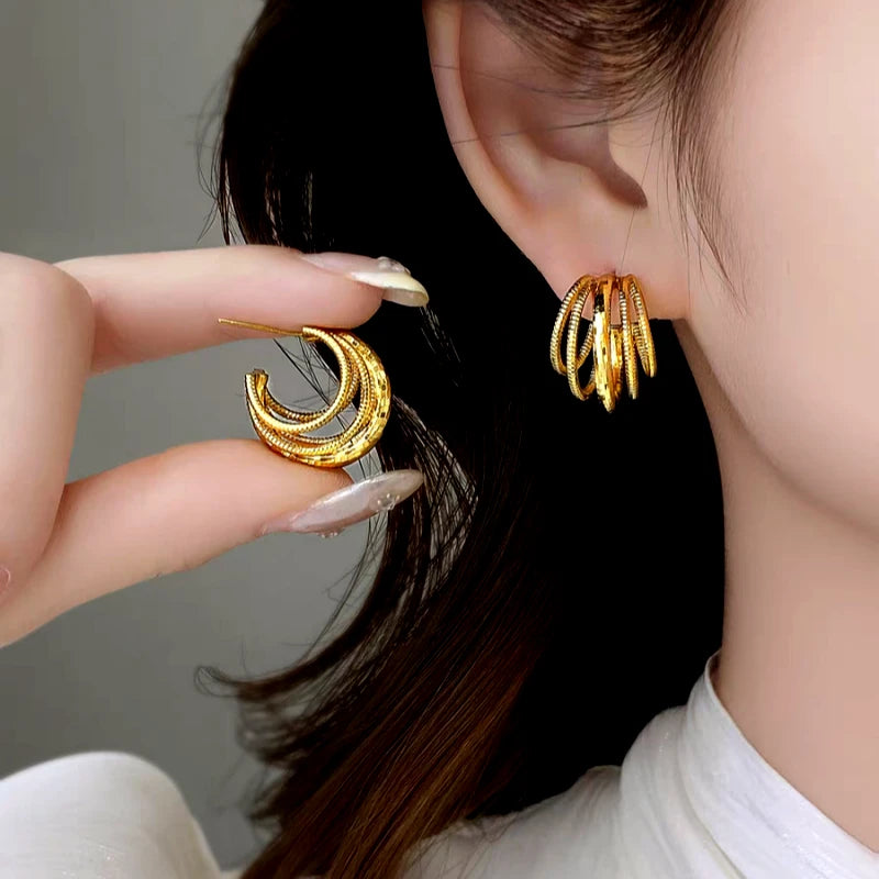 Gold multi-layer hoop earrings: one worn on ear, one held in hand