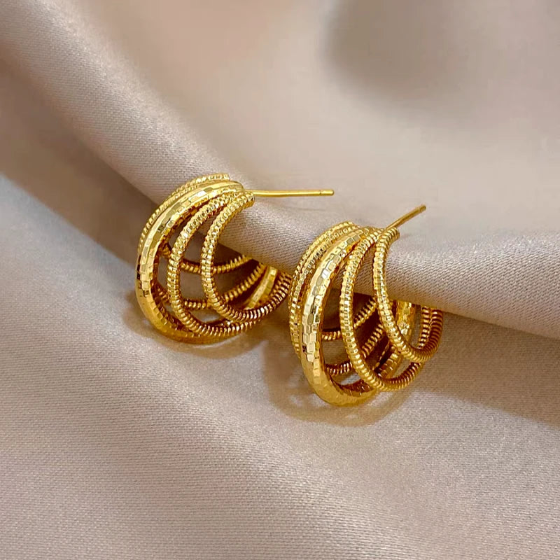 Pair of gold multi-layer C-hoop earrings resting on satin fabric