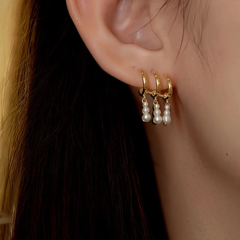 Stacked gold pearl drop huggie earrings worn on human earlobe