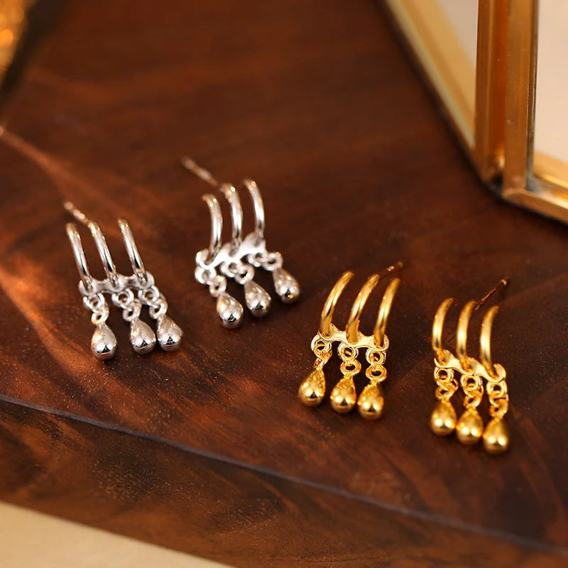 Silver and gold triple teardrop dangle stud earrings on wooden display