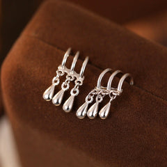 Pair of silver triple-band teardrop dangle ear cuffs on brown velvet jewelry display