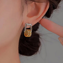 Close-up of silver frame gold layered square hoop earring worn on ear
