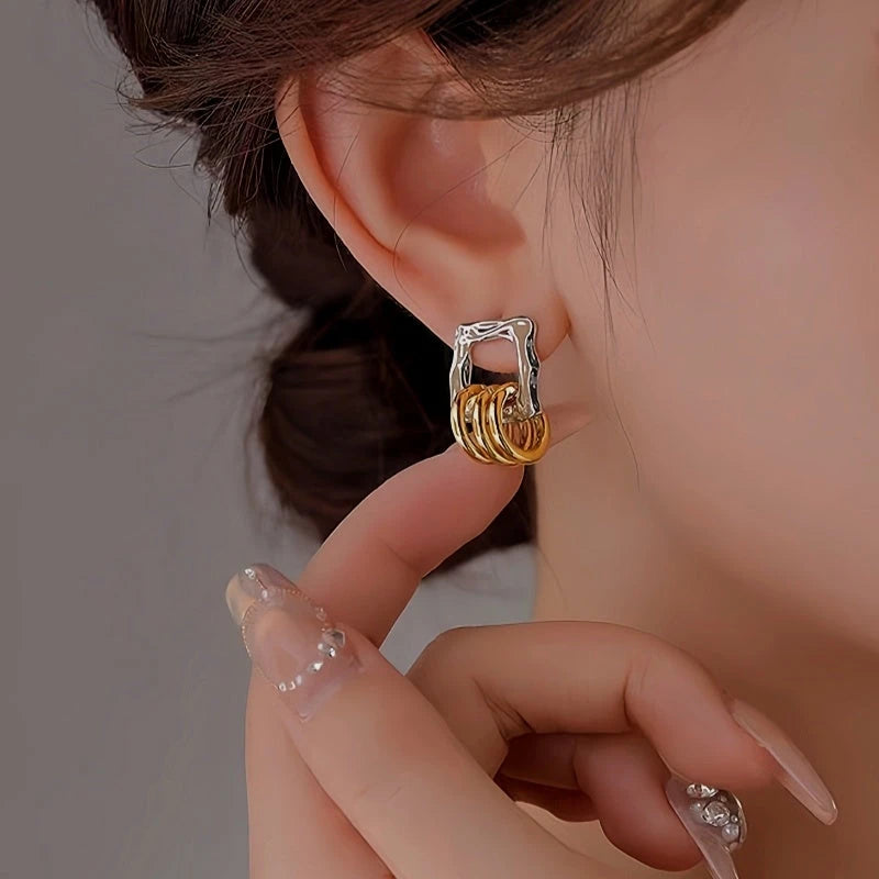Two-tone silver gold stacked square hoop earring on ear, touched by manicured finger