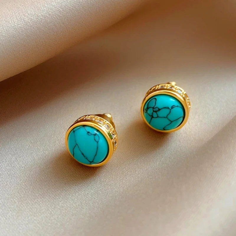 Gold turquoise stud earrings with pave crystal detail on beige satin fabric