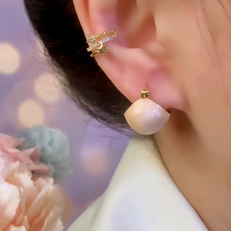 Matching cream teardrop stud earring on ear with layered gold star ear cuff