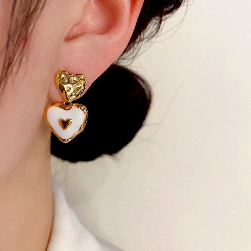 Gold hammered white enamel double heart drop earring worn on woman's ear