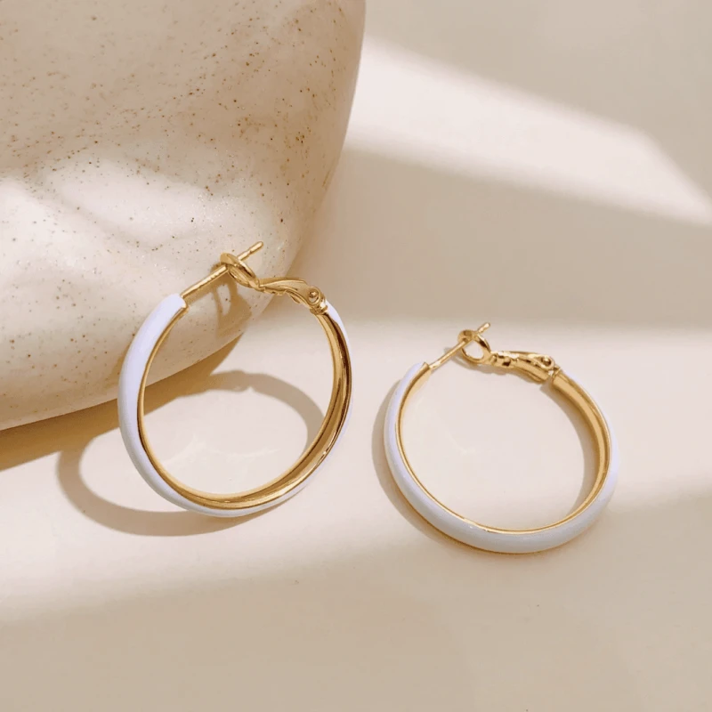 Pair of Gold White Enamel Hoop Earrings on Neutral Beige Background