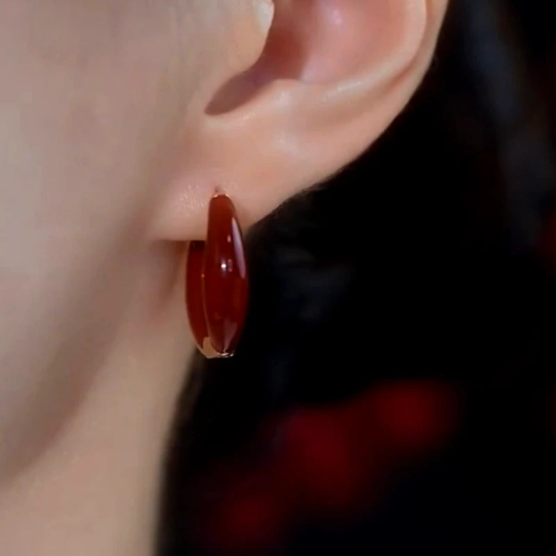 Glossy deep red enamel huggie hoop earring worn on female earlobe close-up