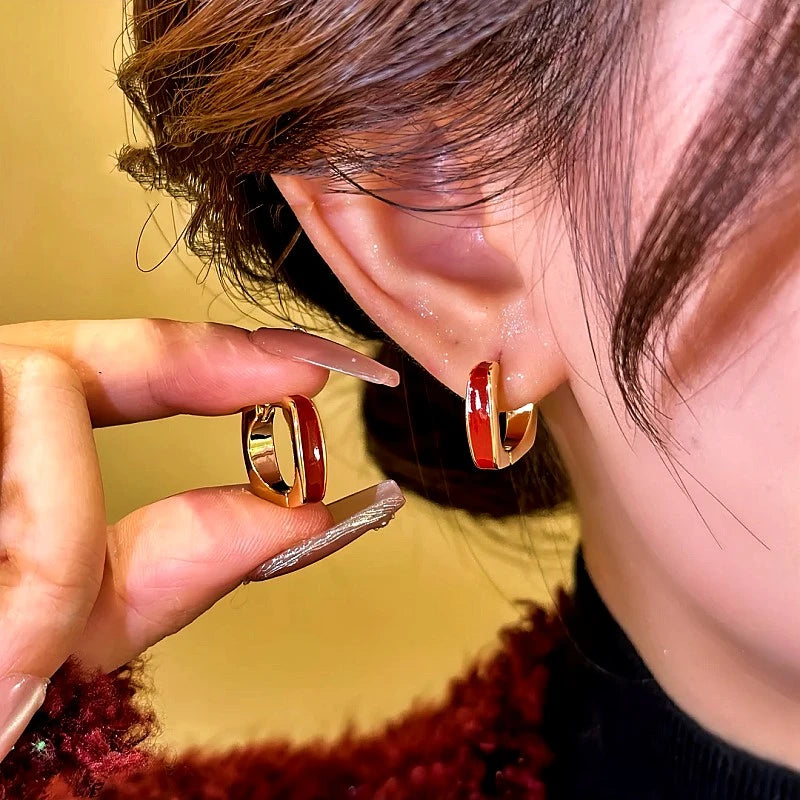 Red enamel gold small hoop earrings, one worn on ear, matching pair held in hand
