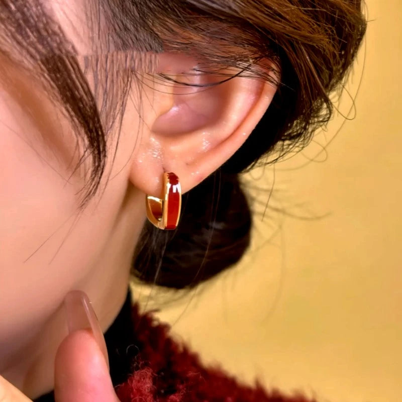 Close-up of red enamel gold small hoop earring worn on ear