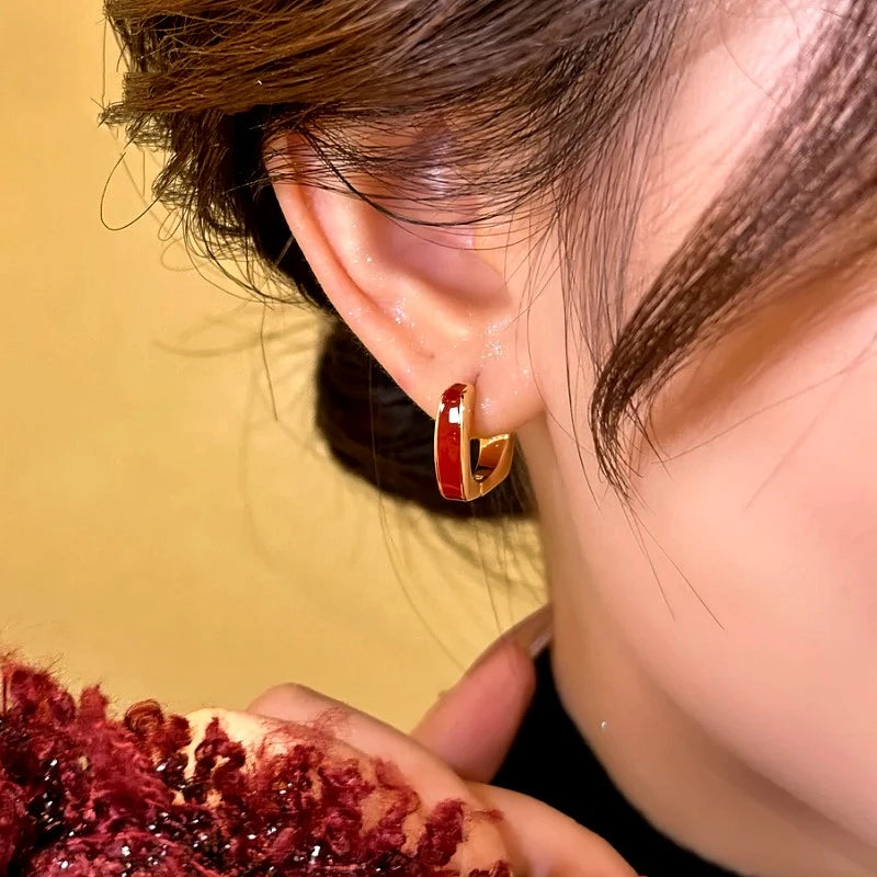Side angle view of red enamel gold small hoop earring worn on ear