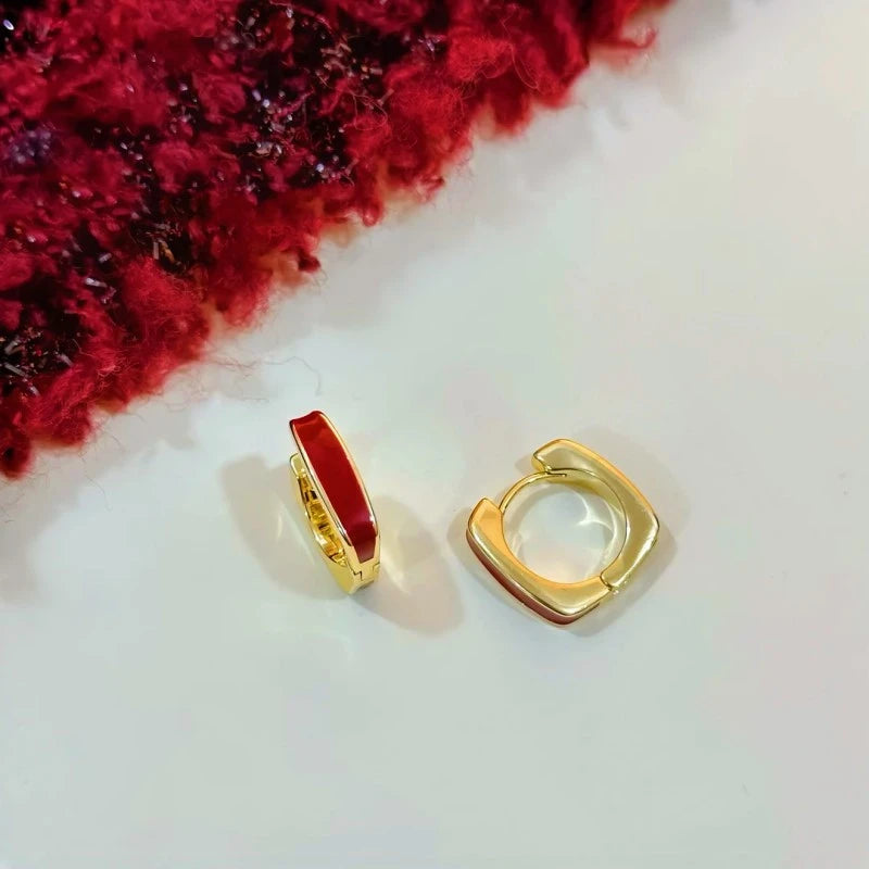 Pair of gold red enamel square huggie hoop earrings on white surface with red knit fabric accent