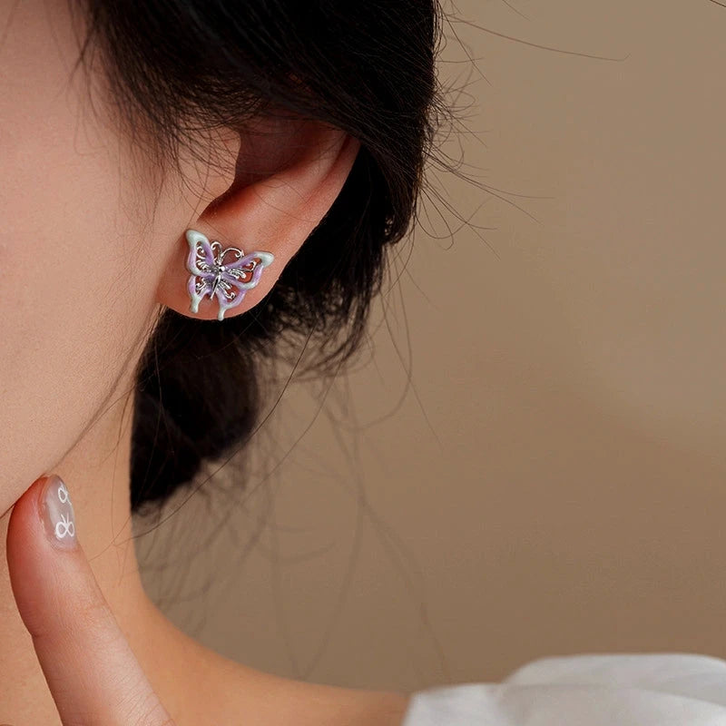 Closeup of purple enamel butterfly stud earring worn on woman's ear