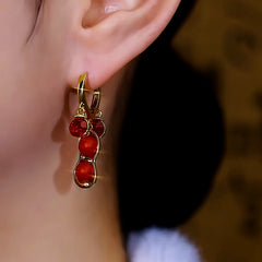Gold red peanut dangle hoop earring worn on woman's ear close up