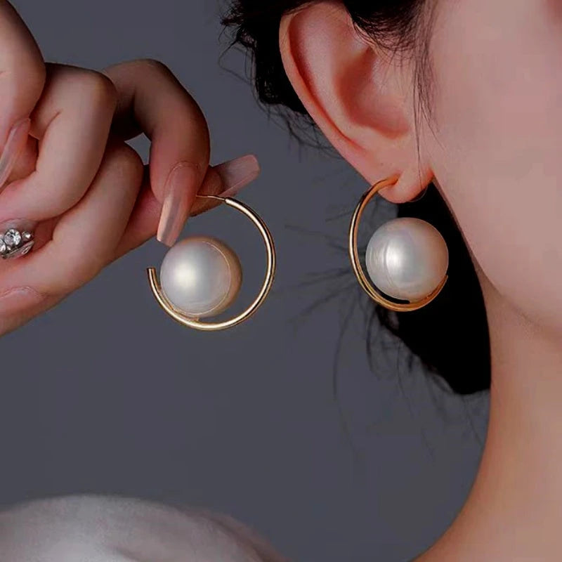 Large white pearl gold open hoop earrings: one worn on ear, one held for detail