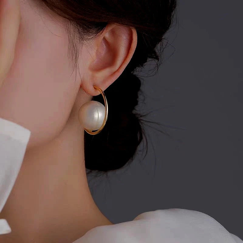 Close-up of large white pearl gold open hoop earring worn on ear, white top visible